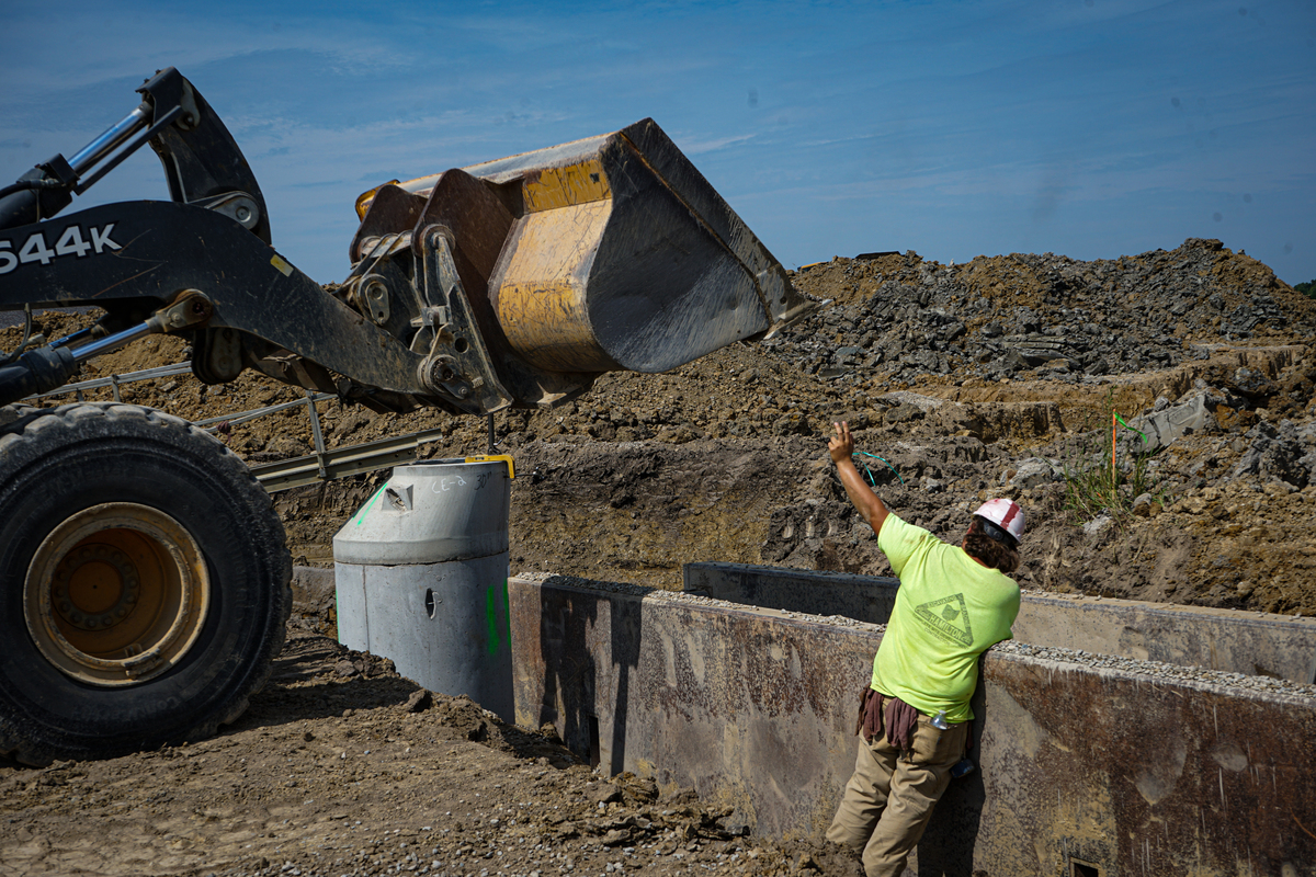 heavy machinery dumping dirt into a trench while a construction worker guides
