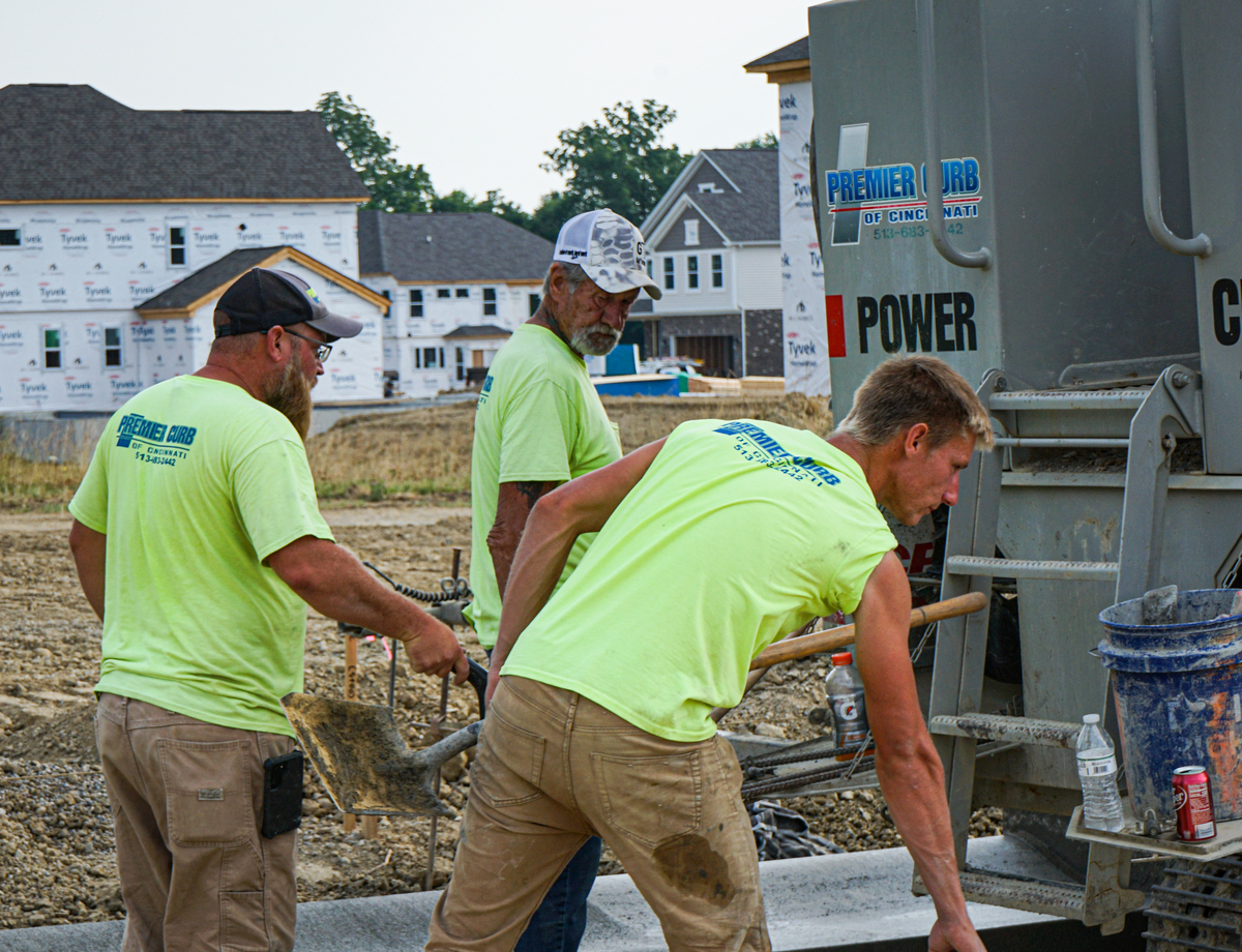 three construction workers in high visibility t-shirts, laying concrete in a subdivision