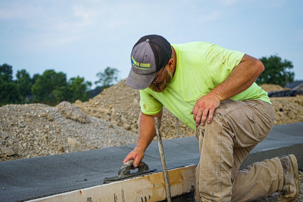 man kneeling, smoothing out freshly poured concrete to make a sidewalk
