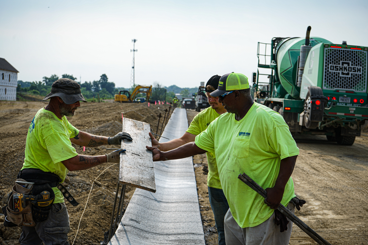 three men holding a piece of concrete, installing a curb