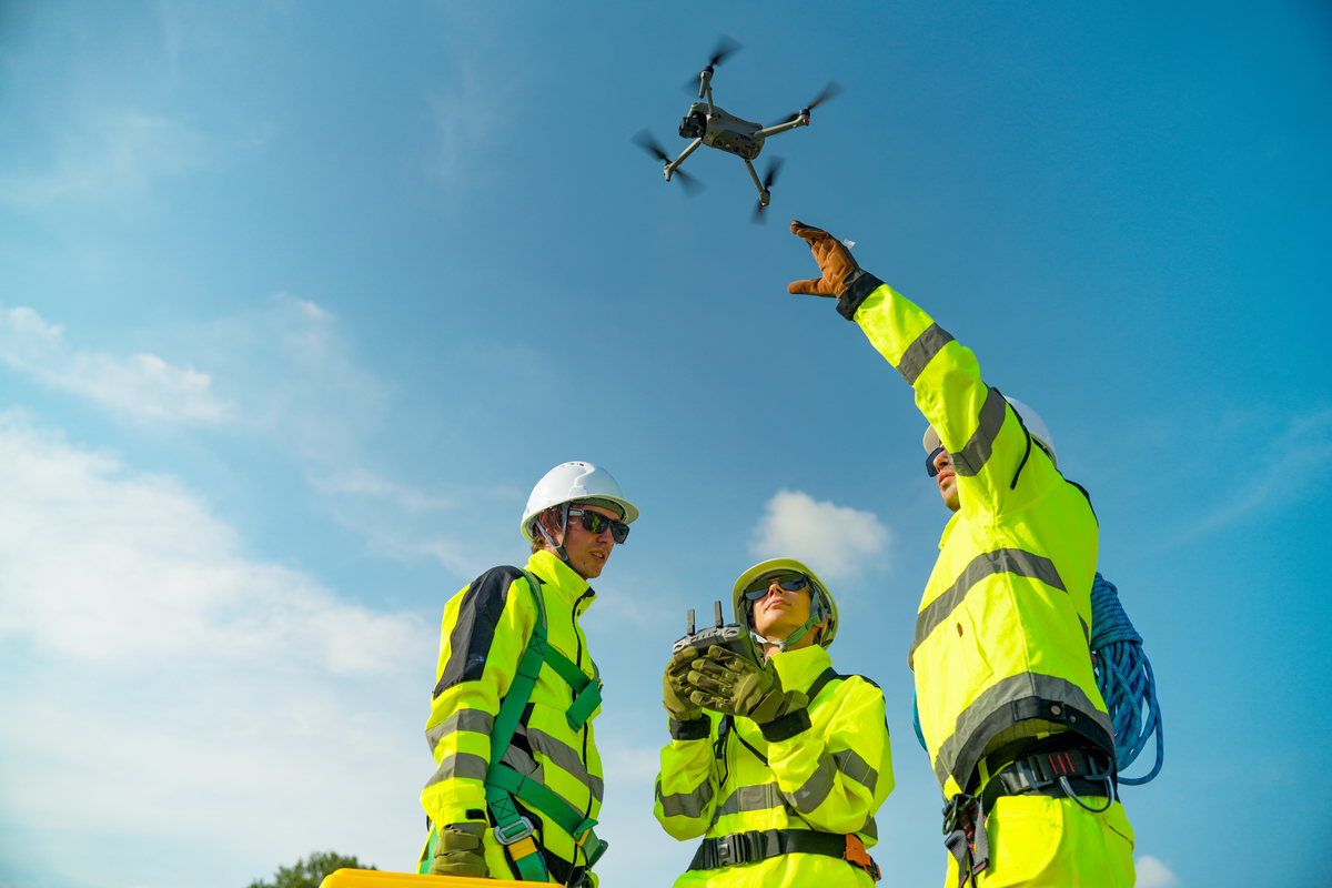 three men in construction gear, flying a drone
